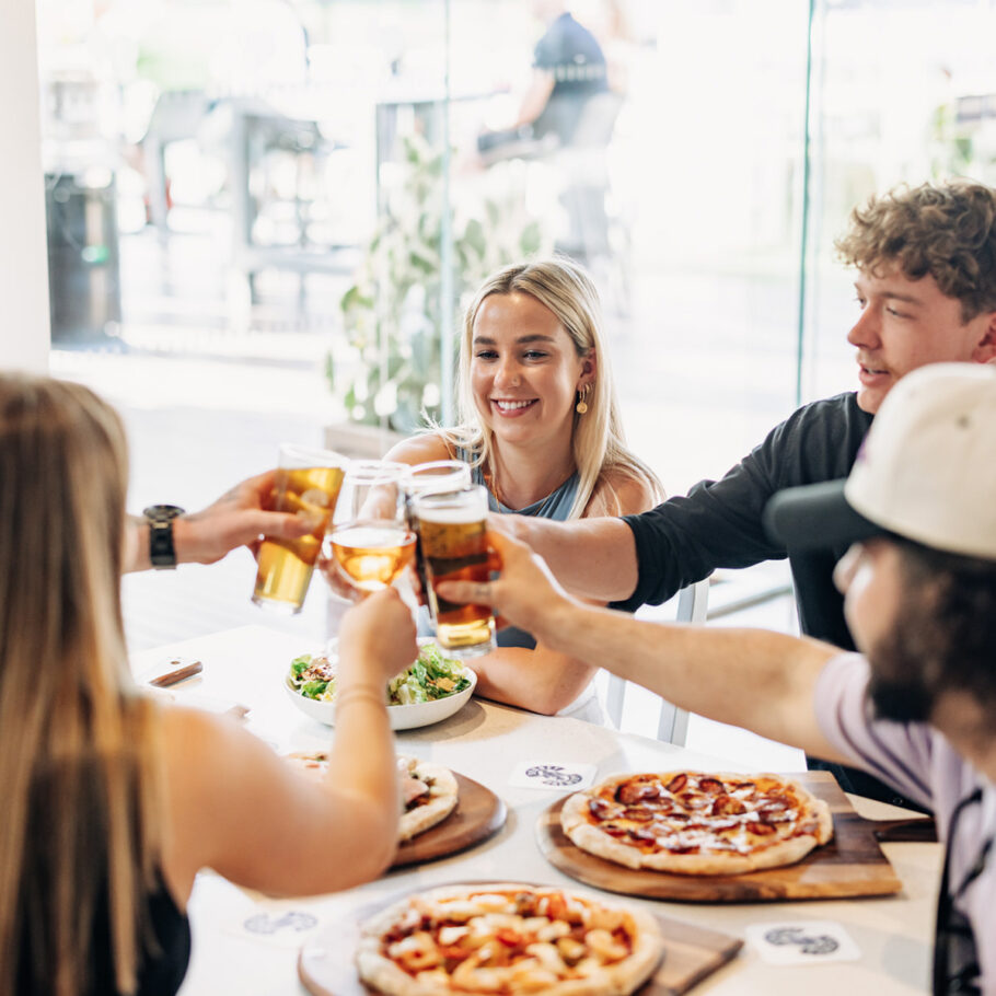 Group of friends clinking drinks over a table of food at Lovedale Bar + Grill